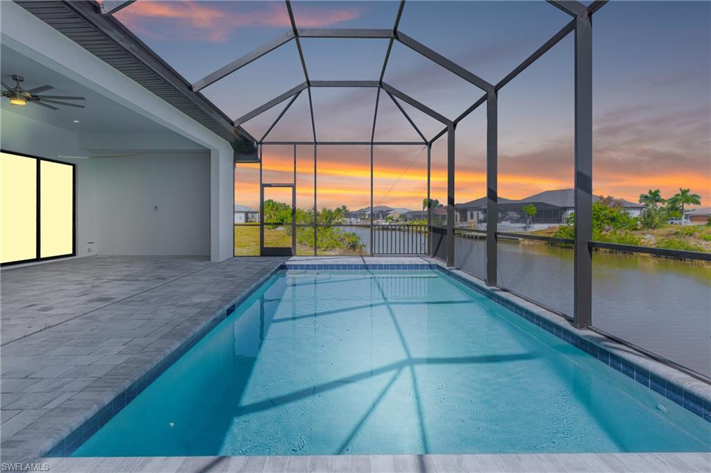 Pool at dusk featuring a sunroom, an outdoor pool, ceiling fan, and a water view