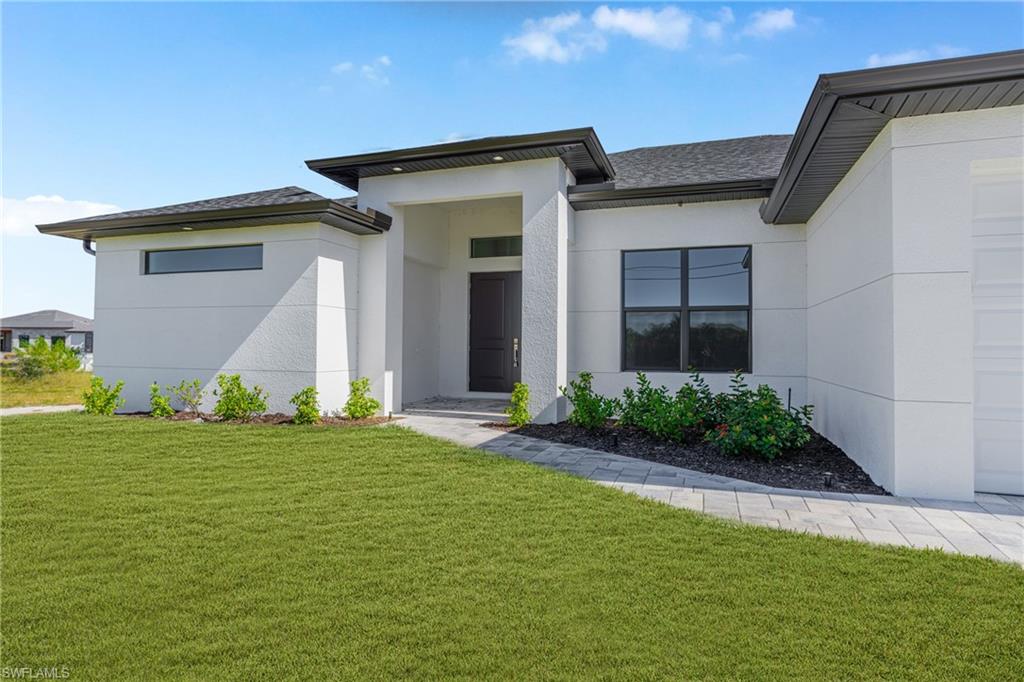 Entrance to property featuring a lawn, stucco siding, and roof with shingles