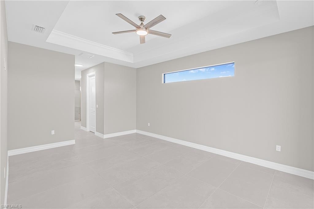 Unfurnished room featuring a raised ceiling, light tile patterned flooring, and a ceiling fan
