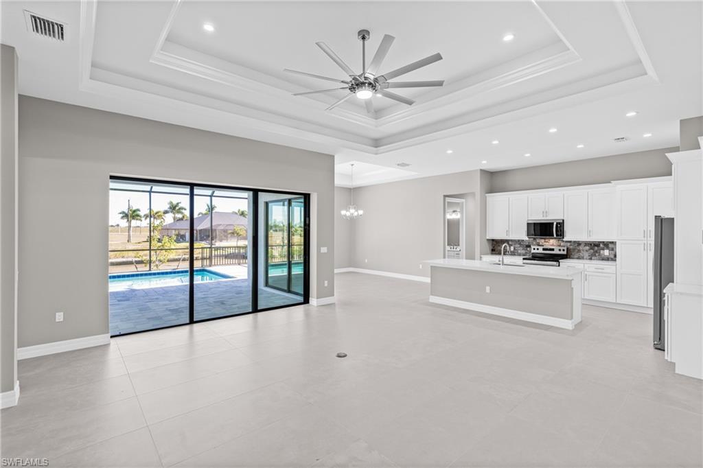 Unfurnished living room featuring a tray ceiling, recessed lighting, a chandelier, a ceiling fan, and light tile patterned floors