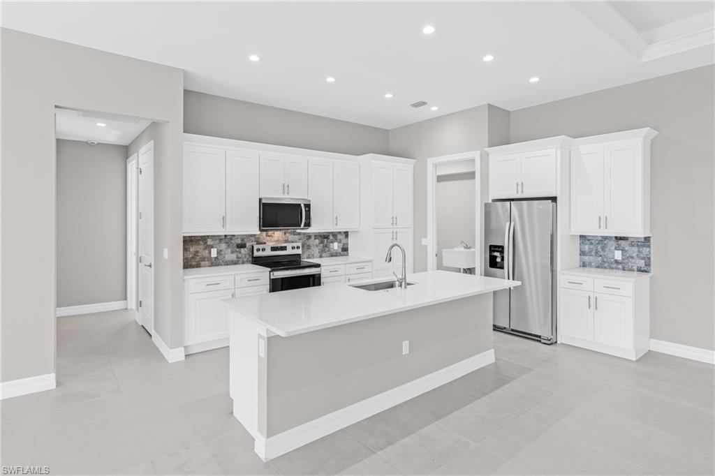 Kitchen with stainless steel appliances, white cabinetry, decorative backsplash, recessed lighting, and an island with sink
