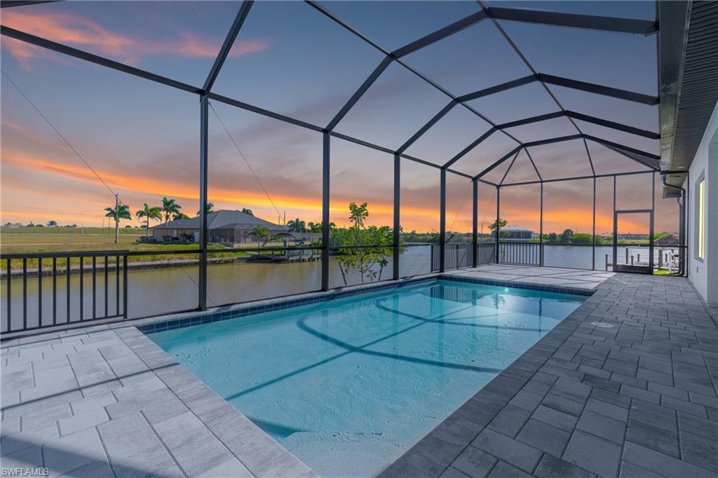 Swimming pool featuring a sunroom, a water view, glass enclosure, and a patio area