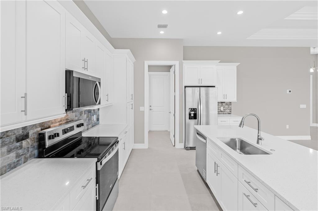 Kitchen featuring backsplash, appliances with stainless steel finishes, white cabinetry, light stone countertops, and recessed lighting