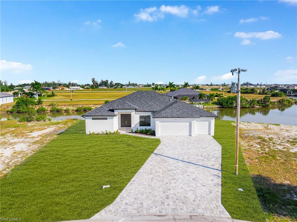 View of front of home featuring a garage, decorative driveway, a front lawn, and a water view