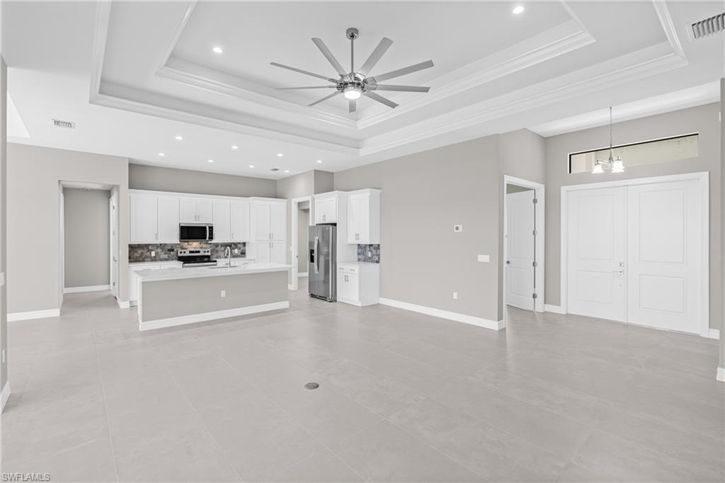 Unfurnished living room featuring ceiling fan, a raised ceiling, light tile patterned floors, a chandelier, and recessed lighting