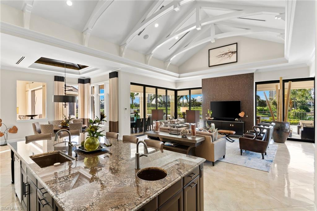 Kitchen with light stone counters, open floor plan, decorative light fixtures, a high ceiling, and an island with sink