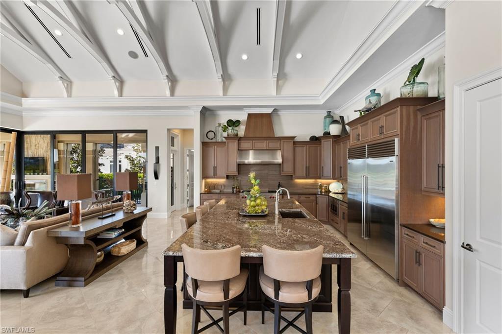 Kitchen with a breakfast bar area, built in refrigerator, dark stone countertops, a spacious island, and open floor plan