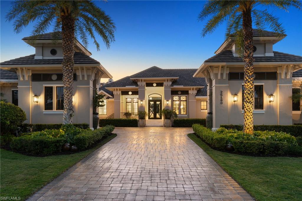 View of front facade featuring stucco siding, a lawn, decorative driveway, and french doors