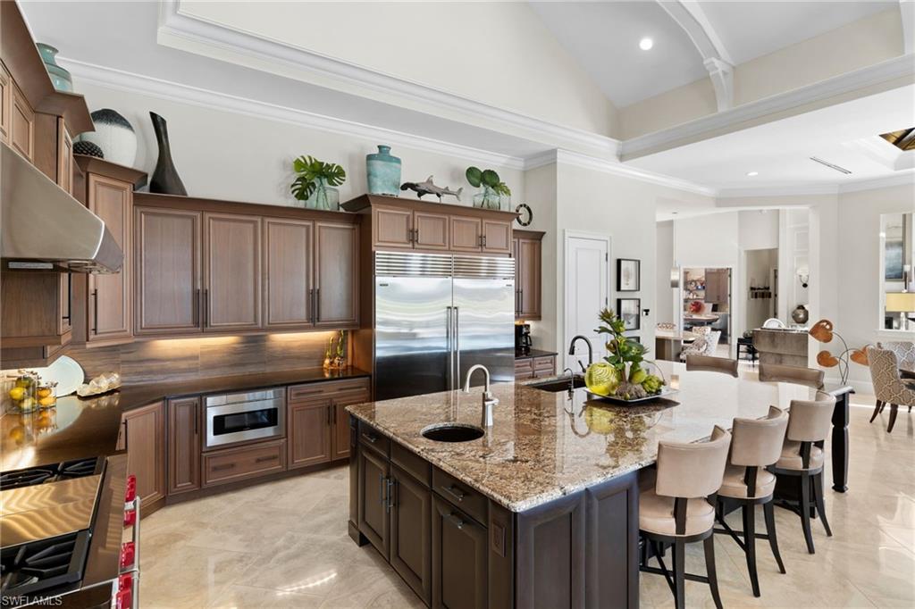 Kitchen featuring crown molding, dark wood finish cabinets, dark stone countertops, built in appliances, and a kitchen island with sink