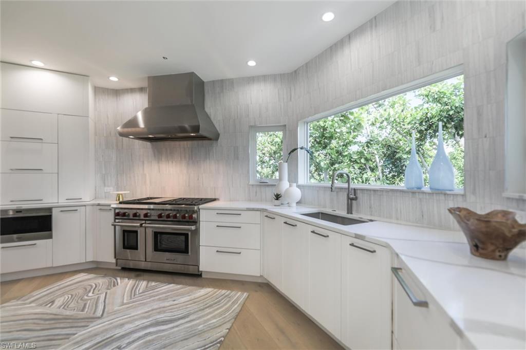 Kitchen featuring light hardwood / wood-style flooring, sink, wall chimney exhaust hood, white cabinetry, and appliances with stainless steel finishes