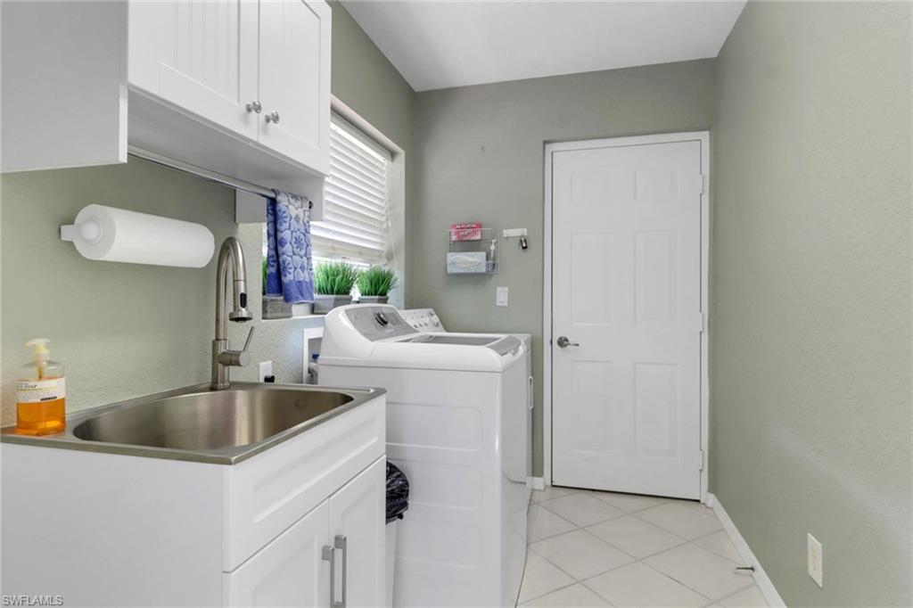 Washroom with light tile patterned flooring, cabinets, separate washer and dryer, and sink