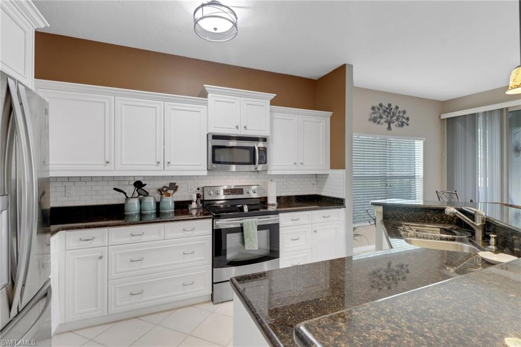 Kitchen featuring appliances with stainless steel finishes, tasteful backsplash, white cabinetry, and sink