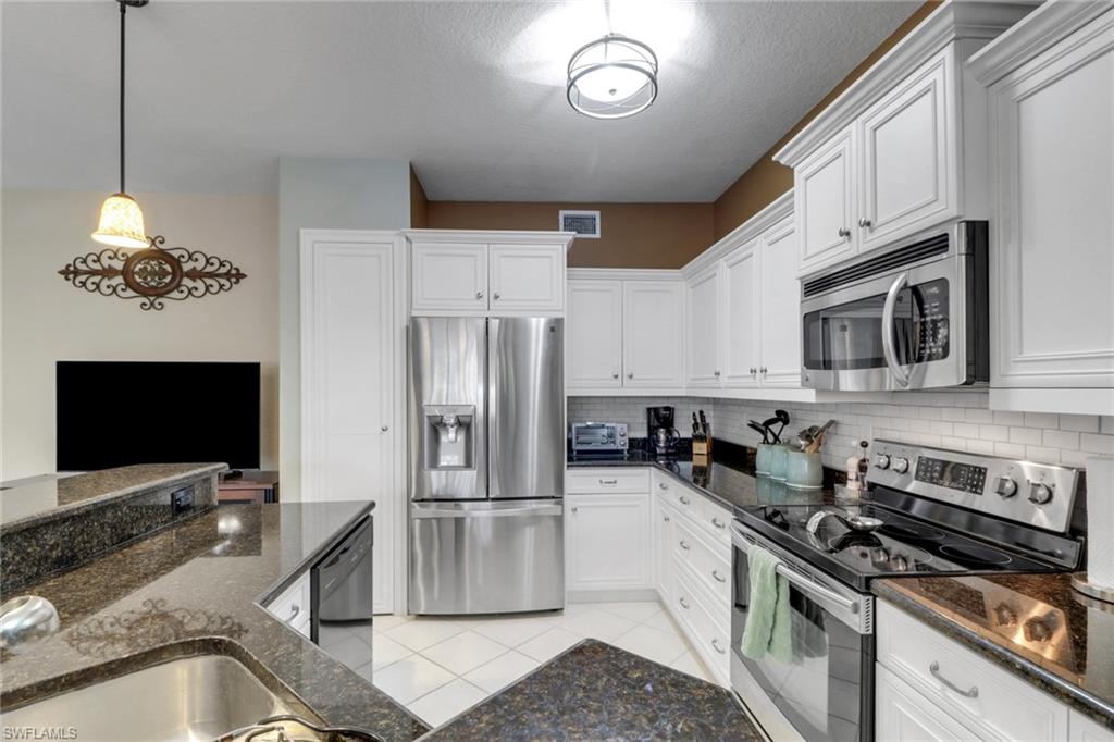 Kitchen with appliances with stainless steel finishes, backsplash, white cabinetry, and dark stone counters