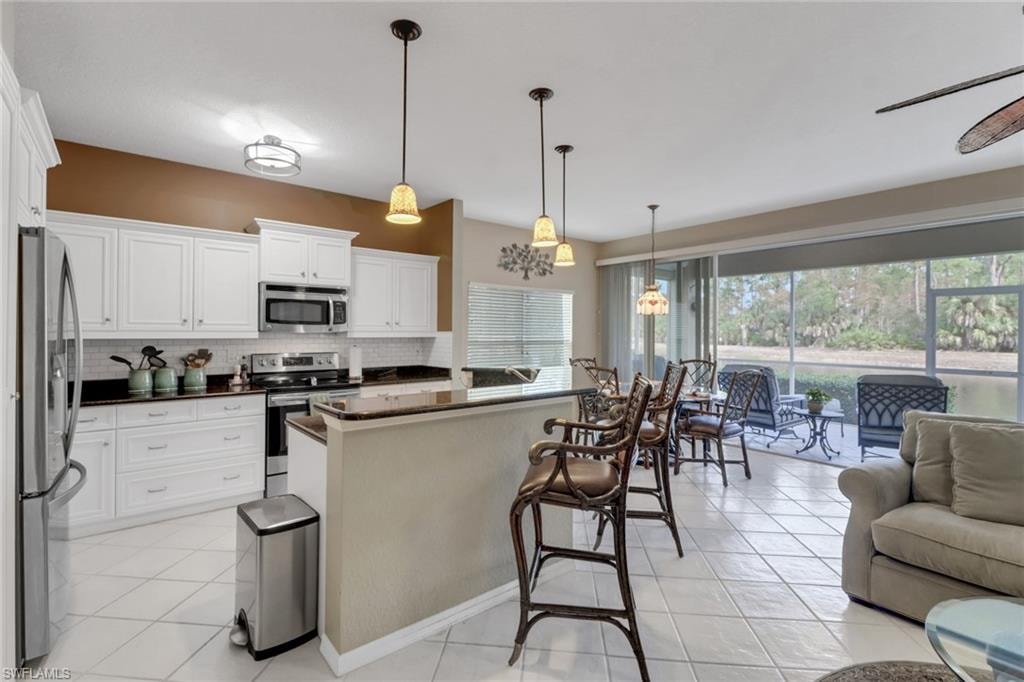 Kitchen with plenty of natural light, white cabinetry, hanging light fixtures, and appliances with stainless steel finishes