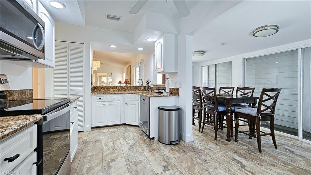 Kitchen with stainless steel appliances, white cabinetry, dark stone countertops, recessed lighting, and lofted ceiling