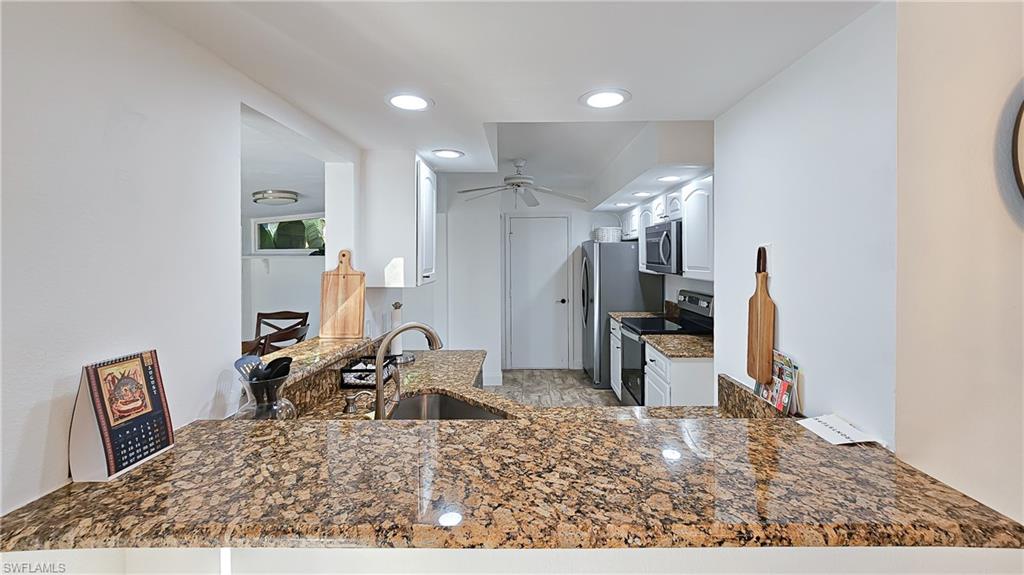Kitchen with appliances with stainless steel finishes, a peninsula, dark stone counters, ceiling fan, and recessed lighting