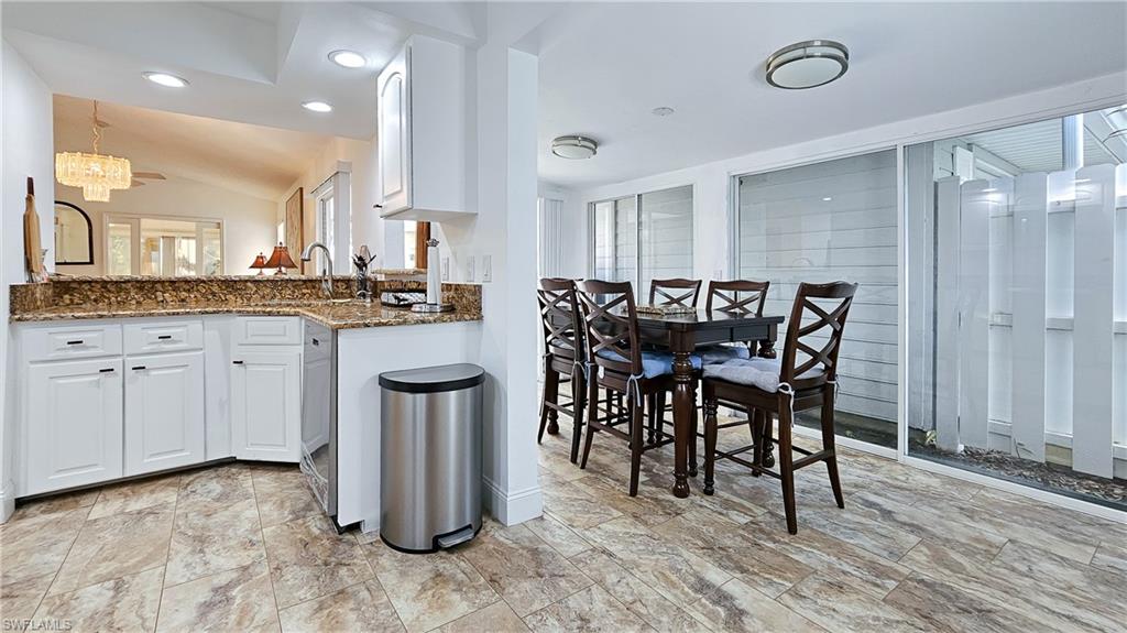 Kitchen featuring dark stone counters, white cabinets, lofted ceiling, a chandelier, and recessed lighting