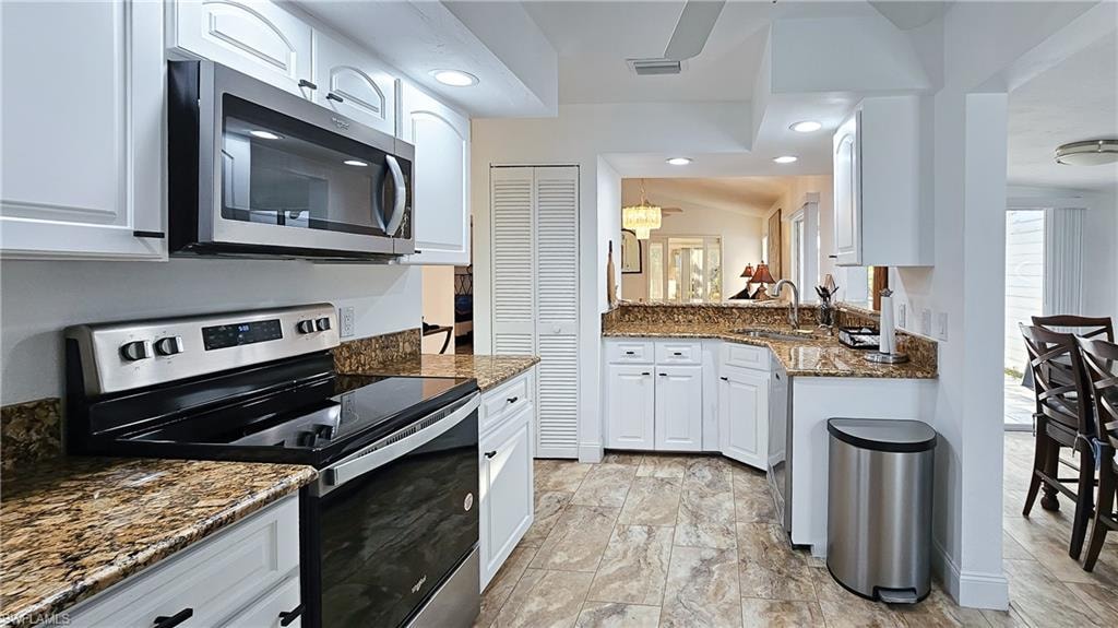 Kitchen with stainless steel appliances, dark stone counters, white cabinets, recessed lighting, and lofted ceiling