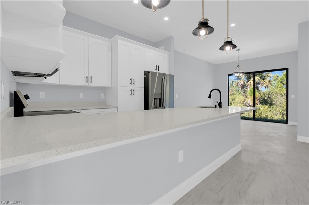 Kitchen featuring a peninsula, light stone counters, stainless steel fridge with ice dispenser, stove, and pendant lighting