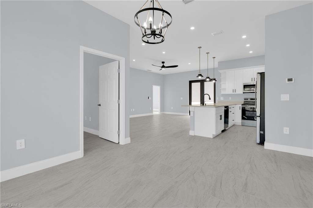 Kitchen featuring open floor plan, white cabinets, a ceiling fan, decorative light fixtures, and a chandelier