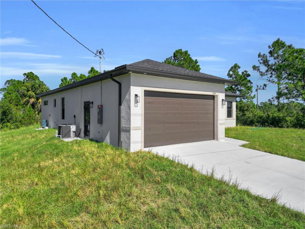 View of side of home with stucco siding, a yard, concrete driveway, and a garage