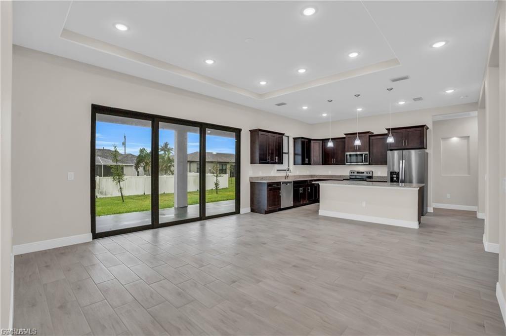Kitchen featuring pendant lighting, a raised ceiling, dark brown cabinets, light wood-style flooring, and a kitchen island
