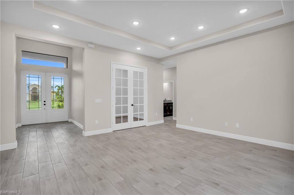 Empty room featuring french doors, a raised ceiling, light wood-style flooring, and recessed lighting