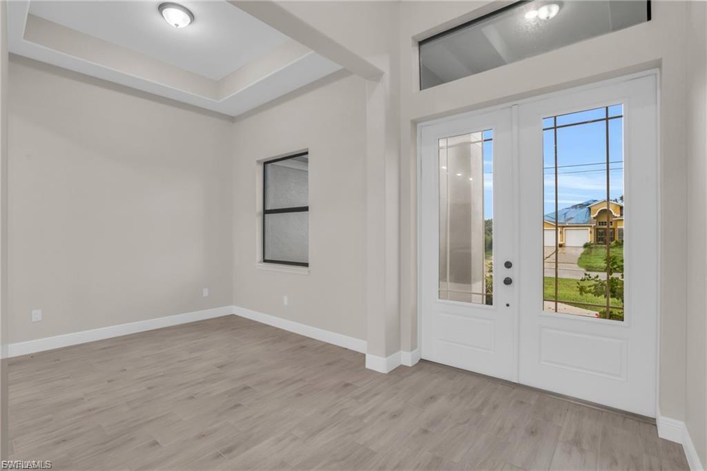 Foyer entrance with light wood-type flooring, french doors, and a tray ceiling