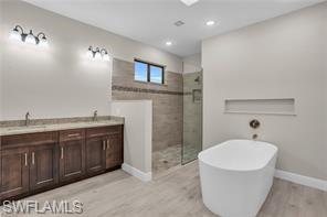 Bathroom featuring double vanity, a soaking tub, light wood finished floors, tiled shower, and recessed lighting