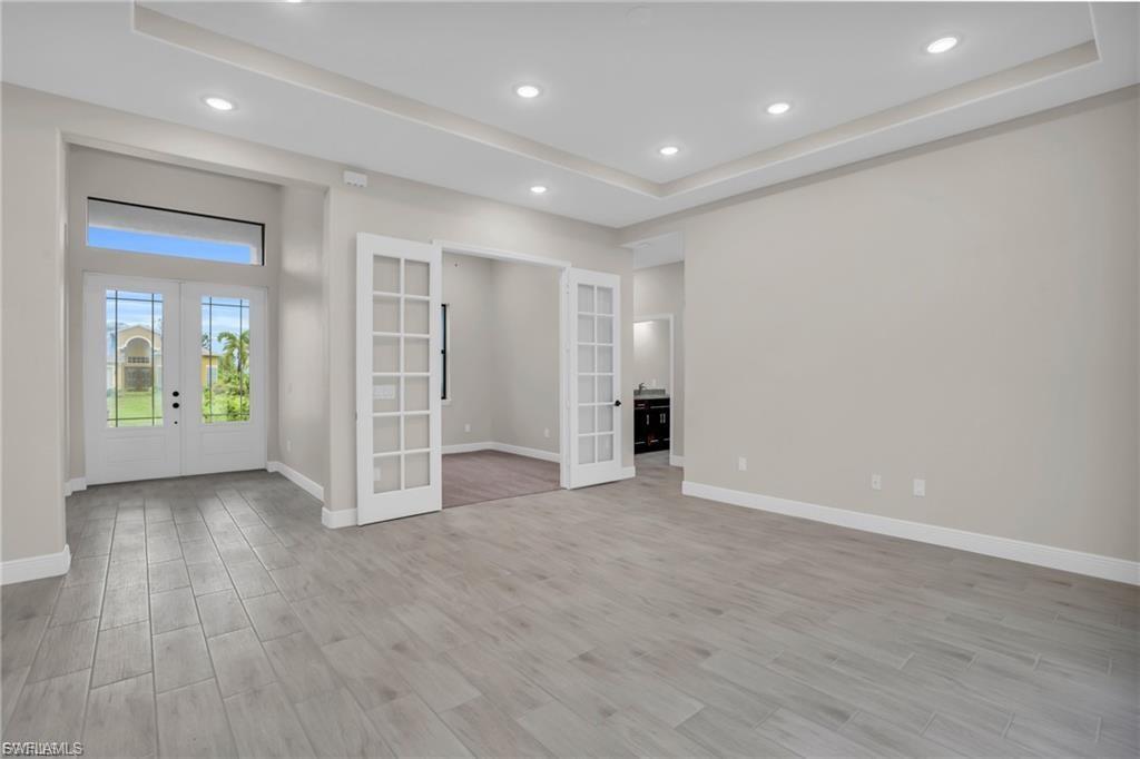 Unfurnished room with french doors, a raised ceiling, light wood-style floors, and recessed lighting