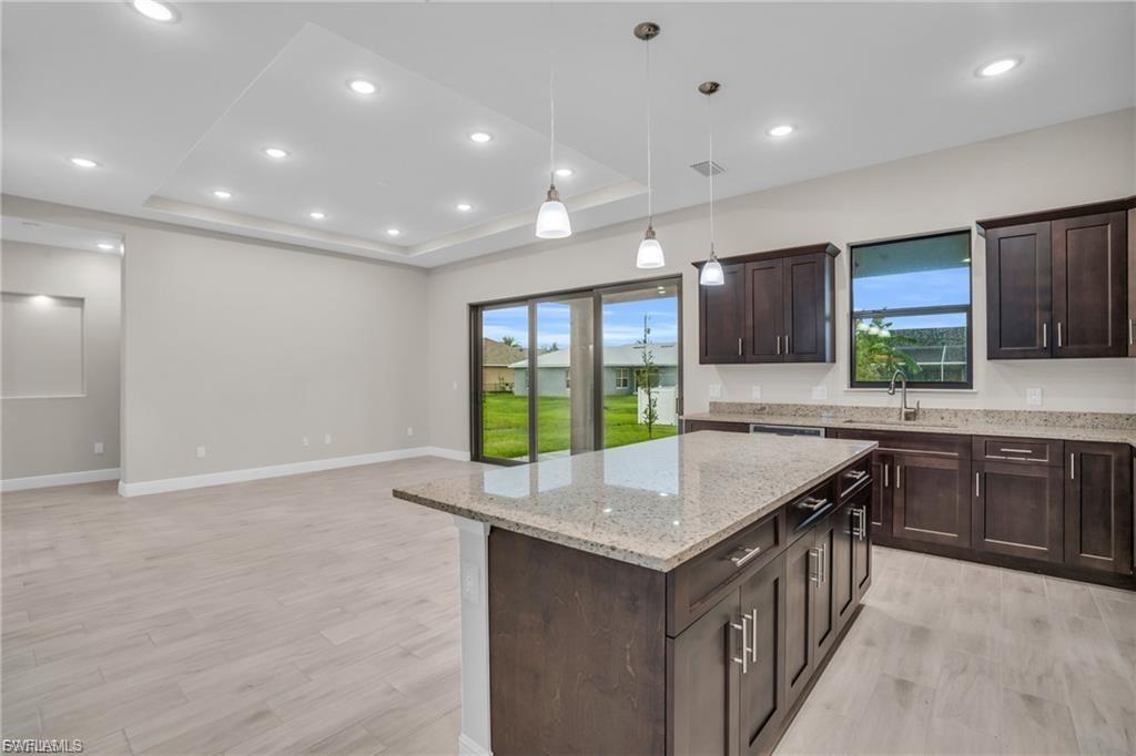 Kitchen featuring a tray ceiling, dark brown cabinetry, decorative light fixtures, light stone counters, and recessed lighting