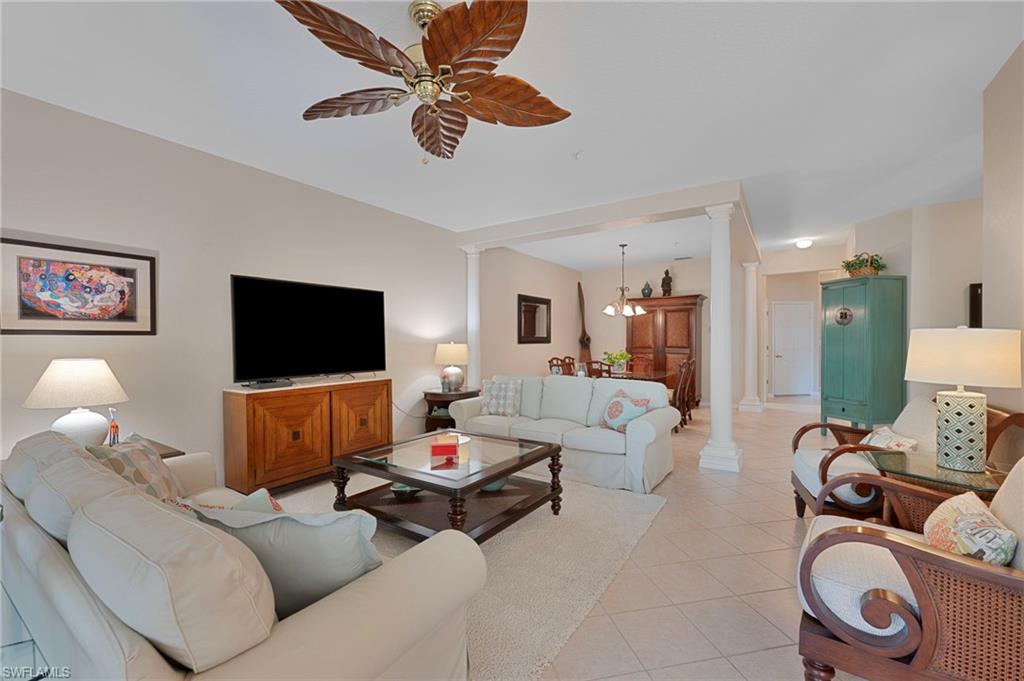 Living room with decorative columns, light tile patterned floors, and a ceiling fan