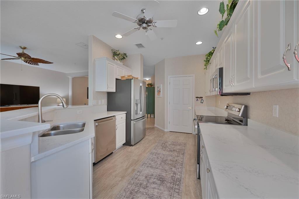 Kitchen featuring a ceiling fan, white cabinetry, stainless steel appliances, light stone countertops, and a peninsula