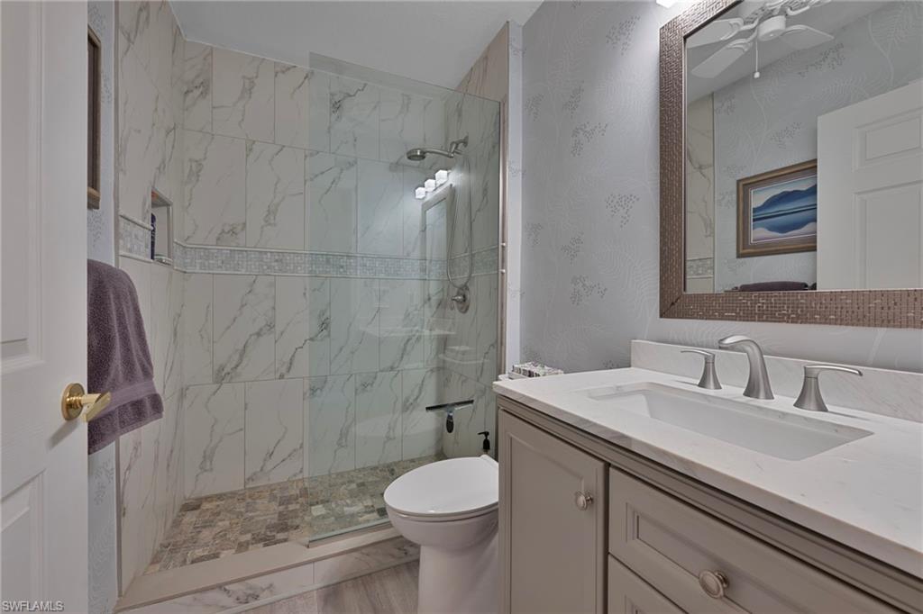 Bathroom featuring vanity, a marble finish shower, ceiling fan, and wallpapered walls