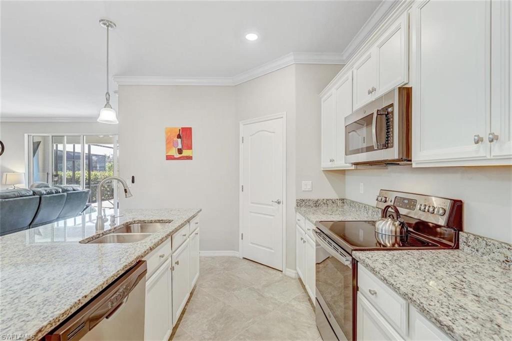 Kitchen with stainless steel appliances, white cabinetry, ornamental molding, open floor plan, and decorative light fixtures