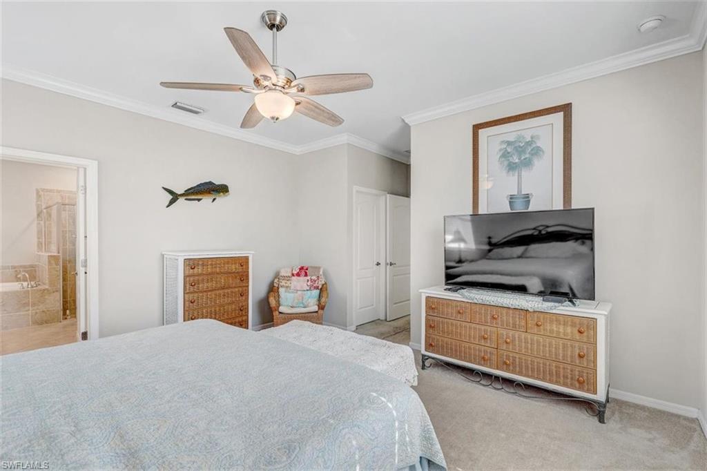Carpeted bedroom featuring ornamental molding, ceiling fan, and ensuite bath