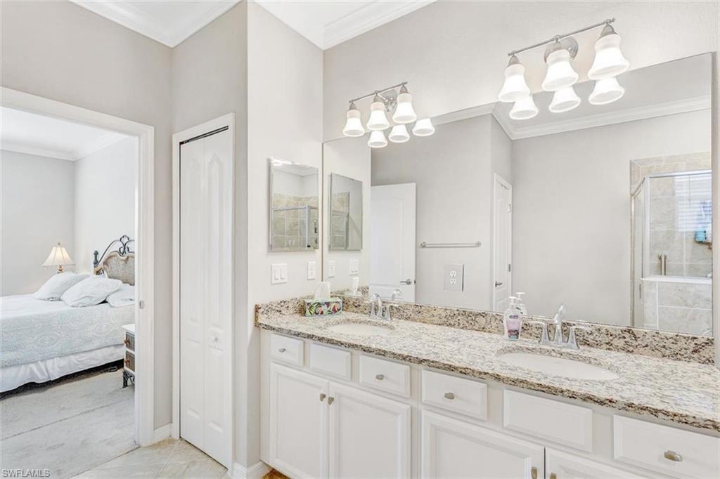 Ensuite bathroom with a closet, ornamental molding, double vanity, a stall shower, and light tile patterned floors