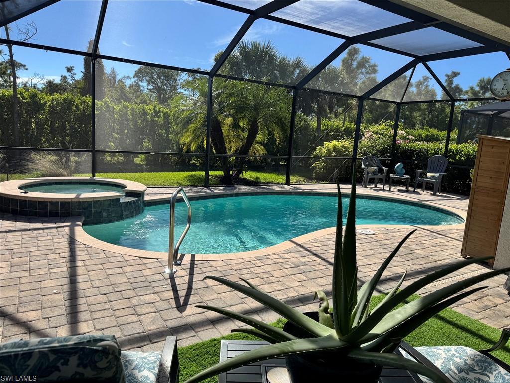 View of swimming pool featuring a sunroom, a pool with connected hot tub, a patio, and glass enclosure