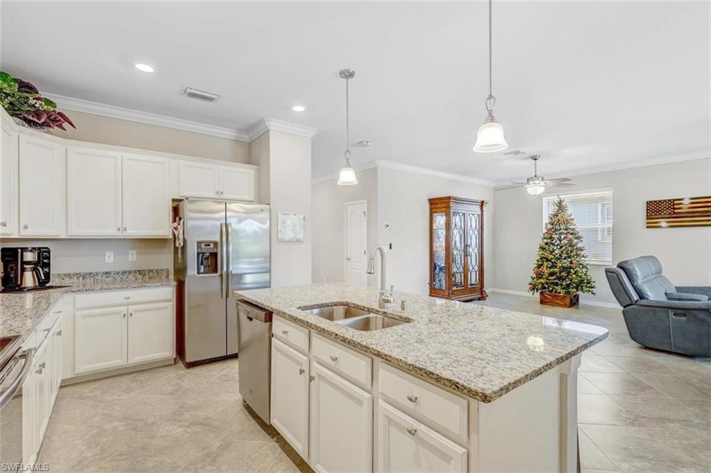 Kitchen featuring white cabinets, open floor plan, ornamental molding, appliances with stainless steel finishes, and hanging light fixtures