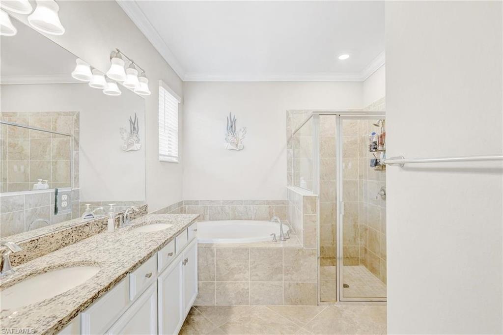 Bathroom with double vanity, a bath, crown molding, a shower stall, and light tile patterned floors