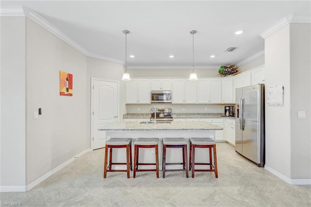 Kitchen featuring stainless steel appliances, crown molding, a kitchen breakfast bar, light stone counters, and decorative light fixtures