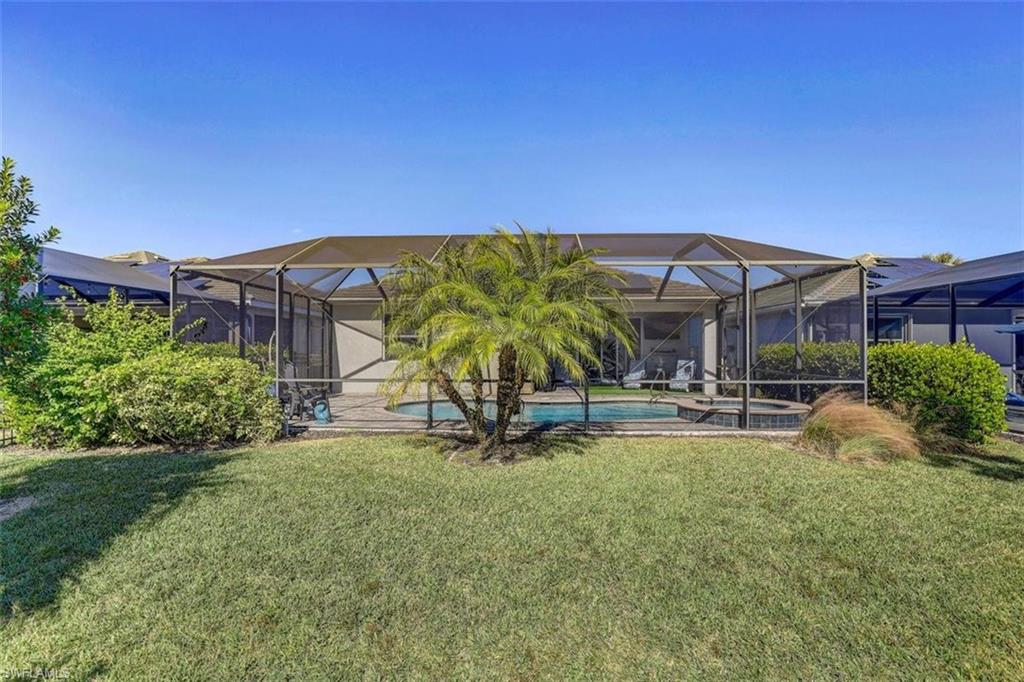 View of green lawn featuring a sunroom, a patio, a pool with connected hot tub, and a lanai