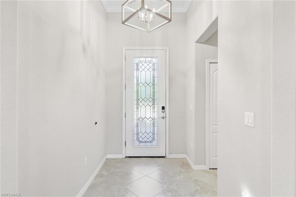 Foyer entrance with light tile patterned flooring, ornamental molding, and a chandelier