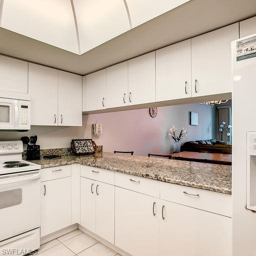 Kitchen featuring white appliances, white cabinetry, light tile patterned flooring, and light stone countertops