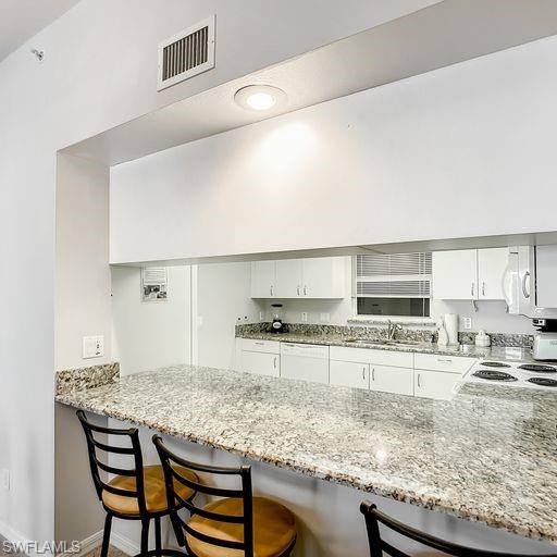 Kitchen featuring white cabinets, light stone counters, and a breakfast bar area