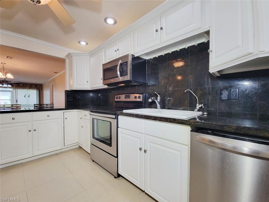 Kitchen featuring backsplash, appliances with stainless steel finishes, ornamental molding, white cabinetry, and light tile patterned flooring
