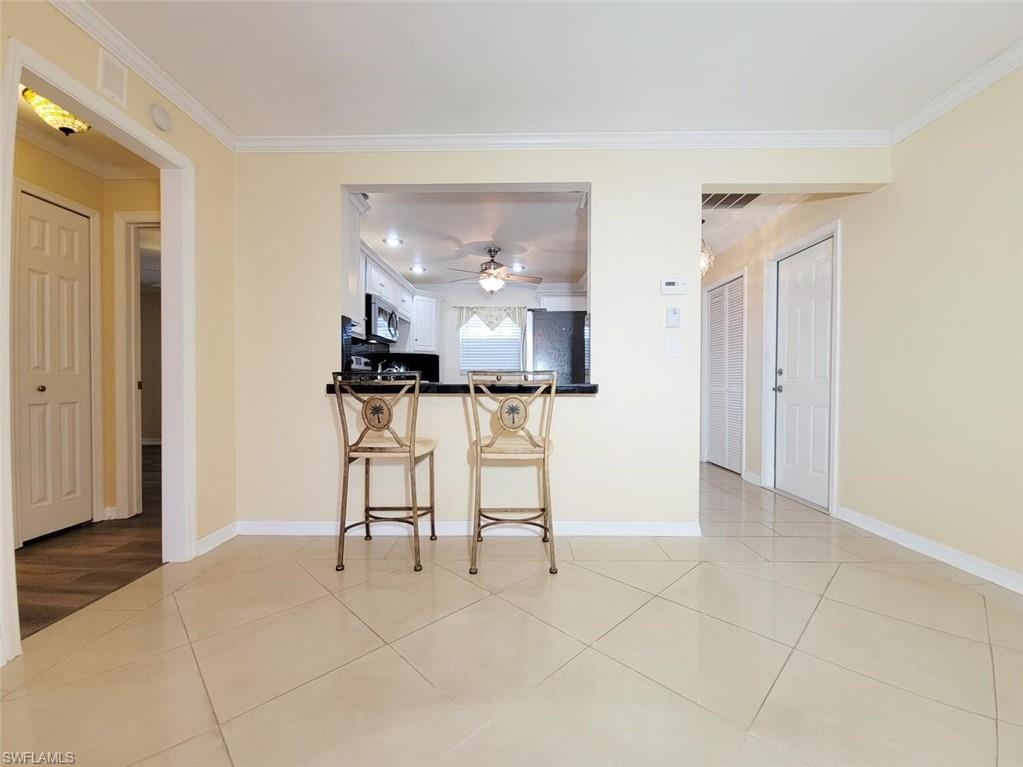 Kitchen with dark countertops, a kitchen bar, stainless steel appliances, light tile patterned flooring, and ornamental molding