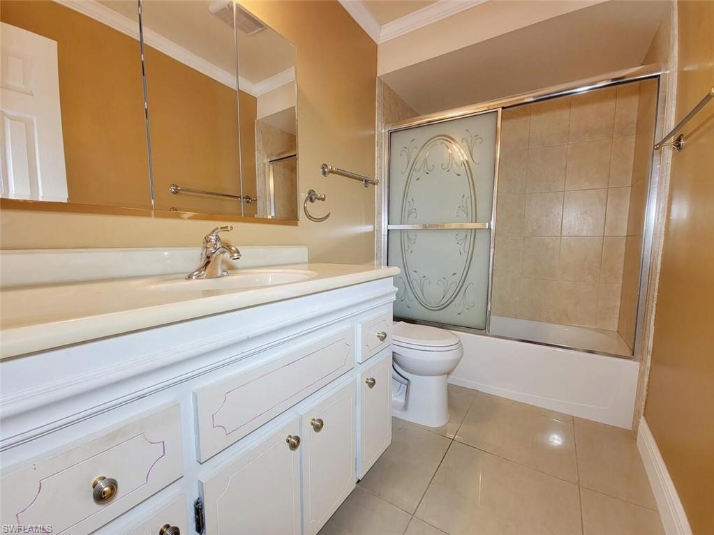 Bathroom with light tile patterned flooring, vanity, ornamental molding, and enclosed tub / shower combo