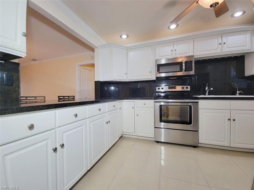 Kitchen featuring decorative backsplash, stainless steel appliances, white cabinets, ornamental molding, and light tile patterned floors