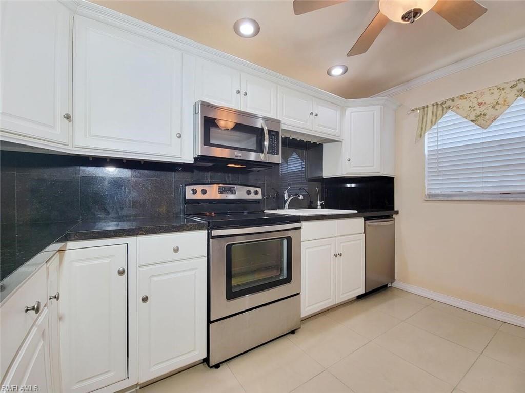 Kitchen featuring decorative backsplash, appliances with stainless steel finishes, white cabinets, crown molding, and light tile patterned floors